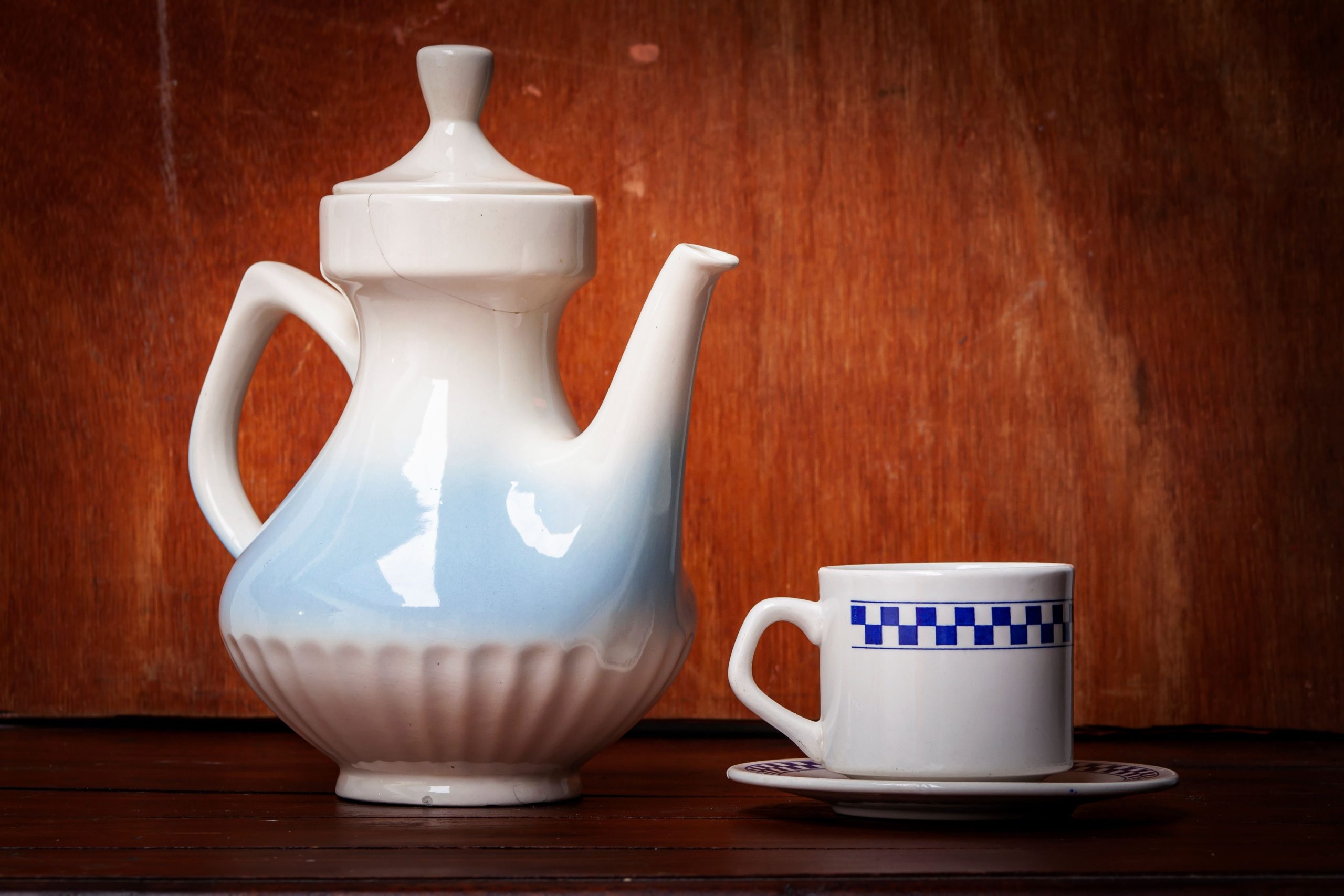 A ceramic teapot with a matching cup on a wooden surface, showcasing classic tableware style.